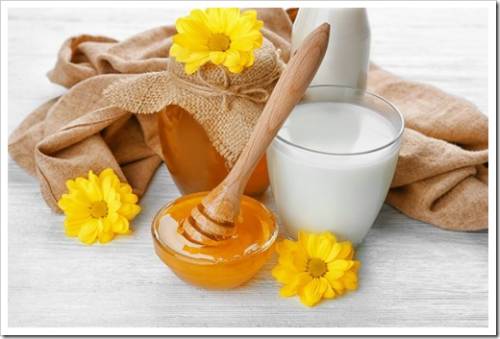 Glass of fresh milk and bowl with golden honey on white wooden table